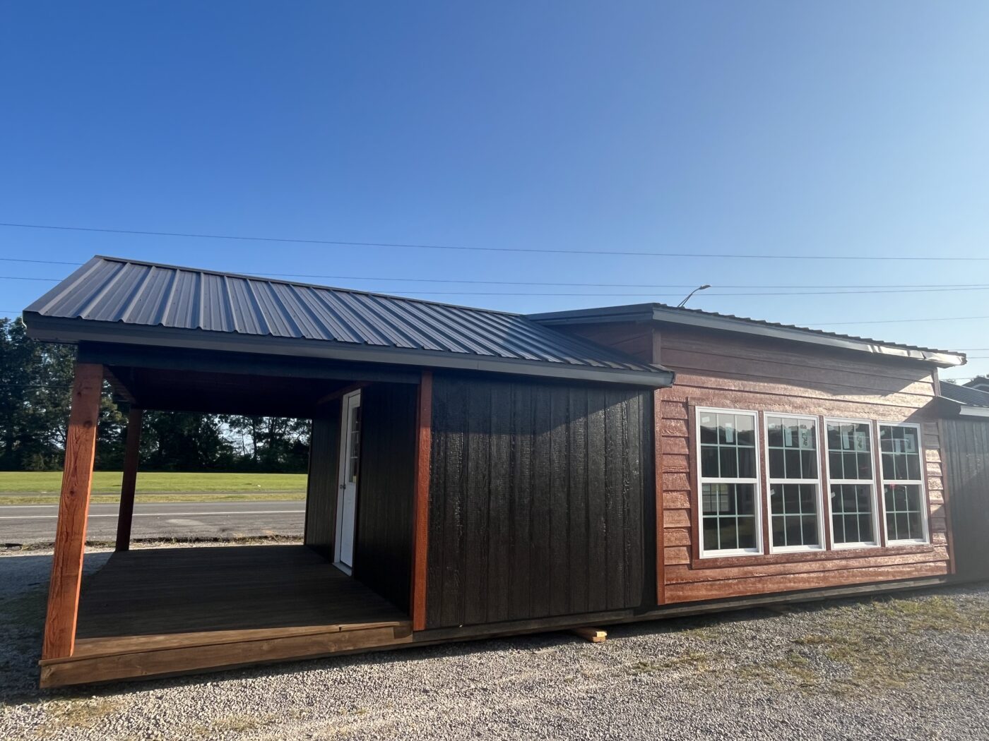 16x40 cabin with brown and orange siding front porch and black metal roof as well as four windws