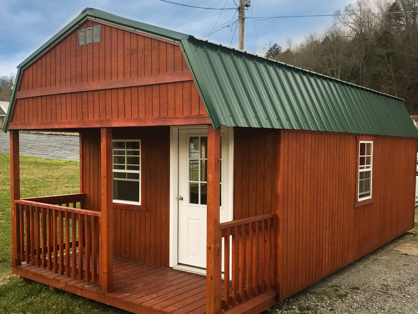 front of log cabin with green metal roof featuring porch white front door and two windows