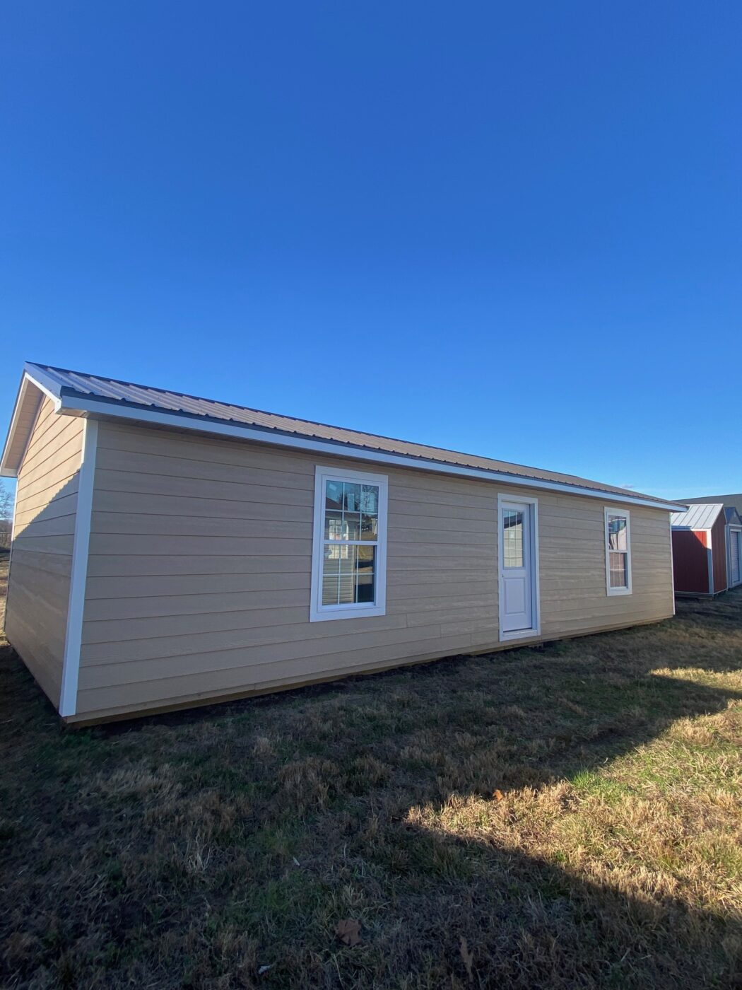 tan 16x40 tiny home shell with white trim two windows and a white front door